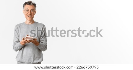 Image of handsome middle-aged man looking surprised and happy, being congratulated with birthday, holding b-day cake and smiling amazed, celebrating over white background.