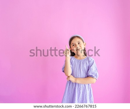 Pretty little girl standing and pointing up with one hand and other arm crossed.