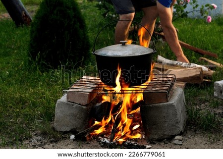 Defocus man cooking fish soup in the iron bowler over a campfire. Fish soup boils in cauldron at the stake. Soup in a pot in the fire. Camp at day. Out of focus.