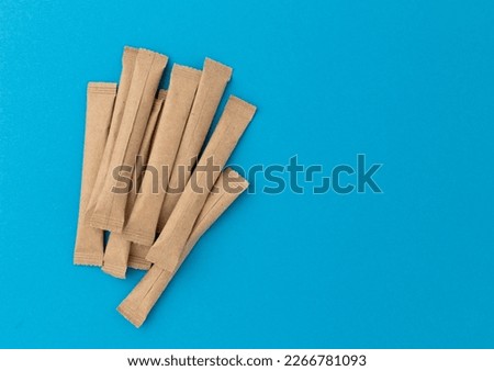 beige sticks of sugar with space for text on blue background, flat lay, top view