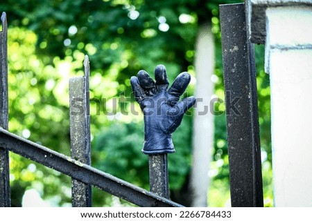 One black leather glove with splayed fingers put on one tip of a fence in a park