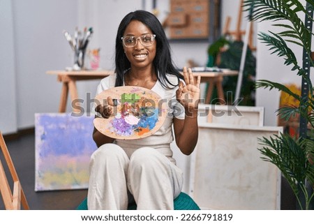 African young woman holding painter palette doing ok sign with fingers, smiling friendly gesturing excellent symbol 