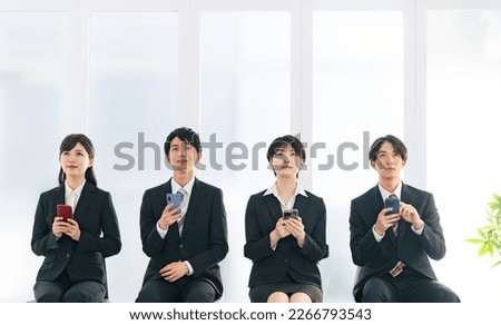 A group of four Asian men and women business people using smartphones.