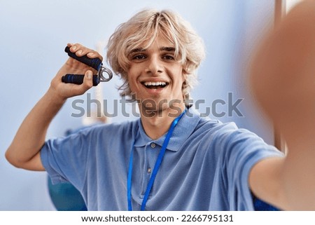 Young blond man pysiotherapist press hand making selfie by camera at rehab clinic