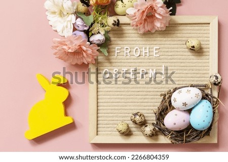 Letter board, Frohe Ostern - Happy Easter in german greeting, Easter eggs and spring flowers on a pastel pink background. View from above. 
