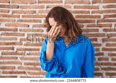 Beautiful brunette woman standing over bricks wall tired rubbing nose and eyes feeling fatigue and headache. stress and frustration concept. 