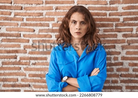 Beautiful brunette woman standing over bricks wall skeptic and nervous, disapproving expression on face with crossed arms. negative person. 