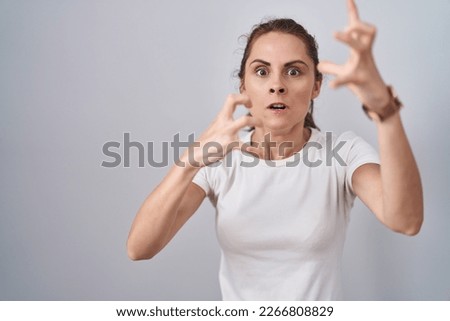Beautiful brunette woman standing over isolated background shouting frustrated with rage, hands trying to strangle, yelling mad 