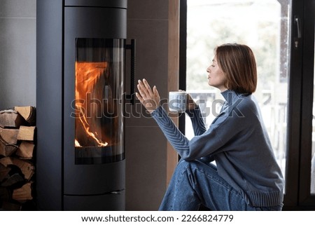 Young attractive woman sits close to fireplace and drinks hot tea in the cozy house Royalty-Free Stock Photo #2266824779