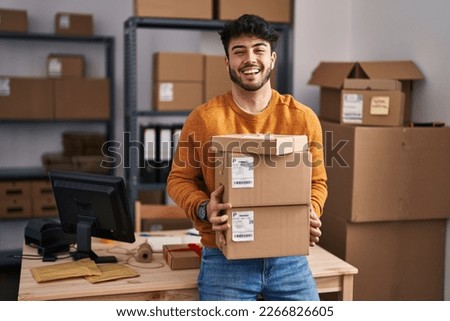 Hispanic man with beard working at small business ecommerce holding packages celebrating crazy and amazed for success with open eyes screaming excited.  Royalty-Free Stock Photo #2266826605