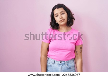 Young hispanic woman standing over pink background looking sleepy and tired, exhausted for fatigue and hangover, lazy eyes in the morning. 