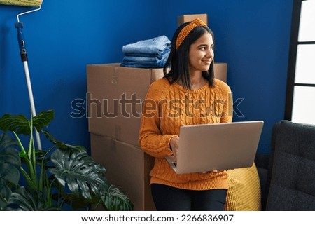Young latin woman smiling confident using laptop at new home