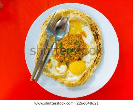 Flatlay picture of "roti sarang burung" on the table. It is paratha looks like bird nest with half cook eggs in the middle with delicious chicken curry.