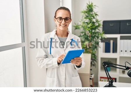 Young blonde woman wearing doctor uniform using touchpad working at clinic
