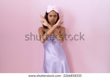 Young hispanic woman wearing sleep mask and nightgown rejection expression crossing arms doing negative sign, angry face 