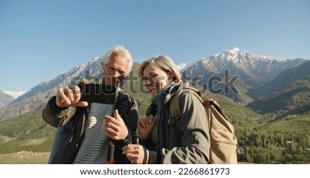 Senior caucasian couple having a nordic walk in mountains, then stopping to take a picture with smartphone. Old people travelling together after retirement - pension, tourism concept 