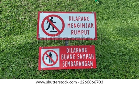 The sign "Dilarang menginjak rumput" atau prohibits stepping on the grass and throwing garbage on the grass