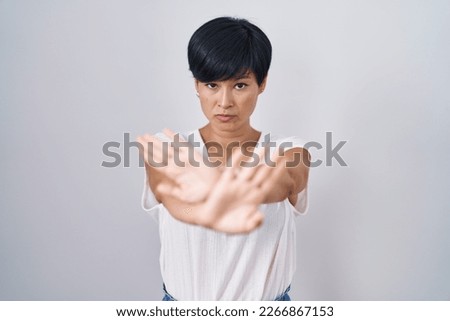Young asian woman with short hair standing over isolated background rejection expression crossing arms and palms doing negative sign, angry face 