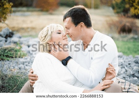 Man hugs woman and almost kisses her while sitting on a blanket on the lawn