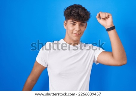 Hispanic teenager standing over blue background dancing happy and cheerful, smiling moving casual and confident listening to music 
