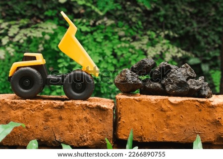After some edits, a photo of a yellow toy dump truck try to carry pile of stones on a brick.
