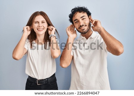 Young couple wearing casual clothes standing together smiling pulling ears with fingers, funny gesture. audition problem 