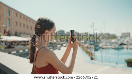 Cute woman takes photos, videos of the seaport on a mobile phone. girl uses social networks and streaming services on a smartphone when shooting yachts and ships
