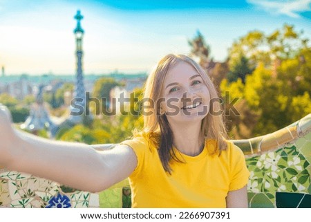 Beautiful young woman looking at camera taking photo with smart phone smiling in Park Guell, Barcelona, Spain. Travel and holidays concept 