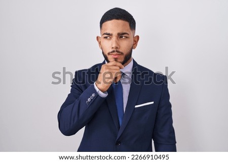 Young hispanic man wearing business suit and tie with hand on chin thinking about question, pensive expression. smiling and thoughtful face. doubt concept.  Royalty-Free Stock Photo #2266910495