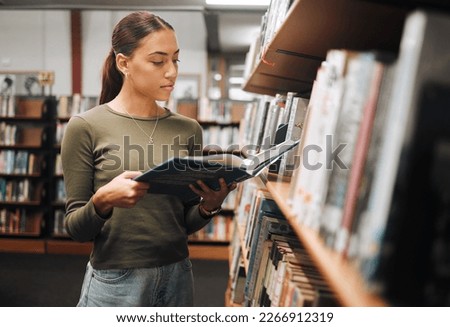 Black woman reading book in a library for education, studying and research in school, university or college campus. Focus, book and student at bookshelf for language learning or philosophy knowledge Royalty-Free Stock Photo #2266912319