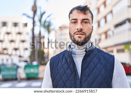 Young hispanic man with serious expression standing at street