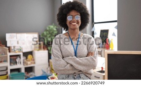 African american woman teacher smiling confident standing with arms crossed gesture at kindergarten