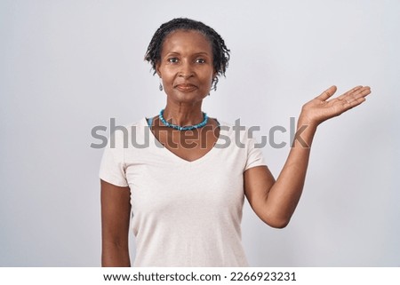 African woman with dreadlocks standing over white background smiling cheerful presenting and pointing with palm of hand looking at the camera. 