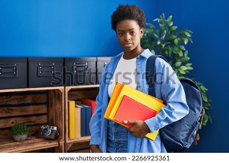 African american woman wearing student backpack and holding books thinking attitude and sober expression looking self confident 