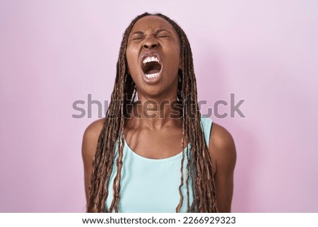 African american woman standing over pink background angry and mad screaming frustrated and furious, shouting with anger. rage and aggressive concept. 