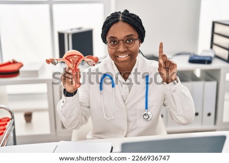 African american doctor woman holding anatomical model of female genital organ surprised with an idea or question pointing finger with happy face, number one  Royalty-Free Stock Photo #2266936747