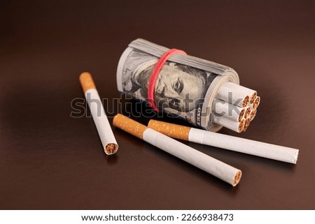 A roll of 100 dollar bills with cigarettes on a black background. Concept of expensive cigarettes.