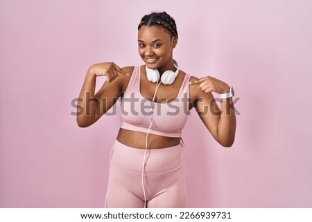 African american woman with braids wearing sportswear and headphones looking confident with smile on face, pointing oneself with fingers proud and happy. 