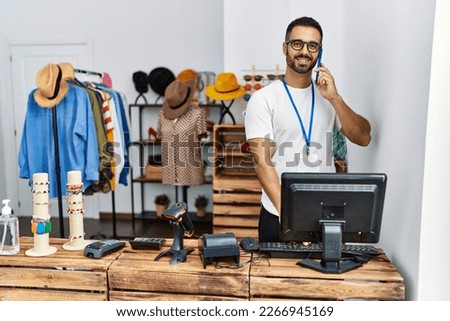 Young hispanic man shopkeeper talking on the smartphone working at clothing store