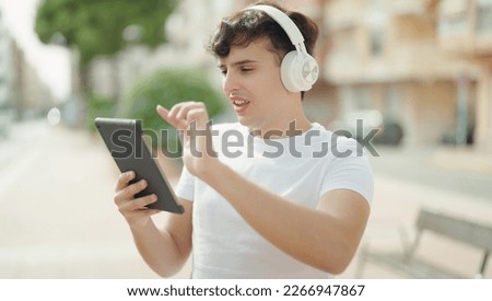Non binary man smiling confident using touchpad and headphones at park