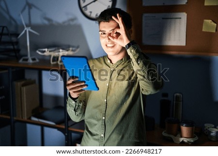 Non binary person using touchpad device at night doing ok gesture with hand smiling, eye looking through fingers with happy face. 