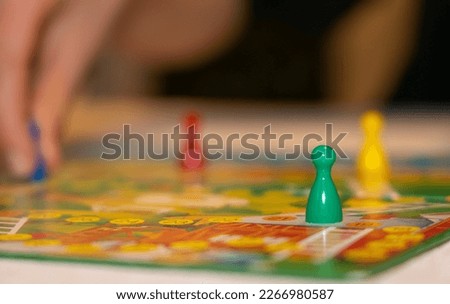 close up view of a board game with colorful game pieces -  focus on one game piece with reduced field of depth. Blurred foreground and blurred background. Blurred Players hand moving a piece