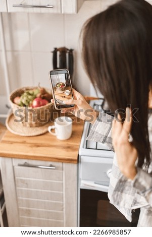 Young long hair Asian woman photographing with smartphone her healthy food and cozy interior of kitchen