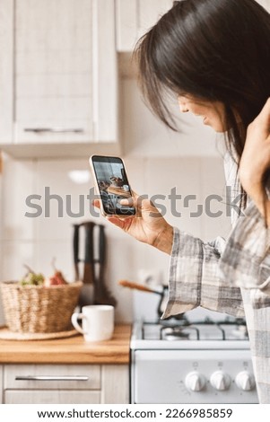 Young beautiful Asian woman using smartphone making digital picture on screen of healthy food, diet at cozy kitchen