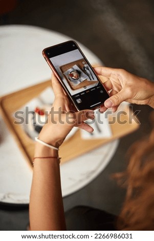 Woman hands snapping ball of ice cream on brownie decorated with strawberries on plate with mobile phone. Hand taking digital photo, picture of dessert food using smartphone. View screen