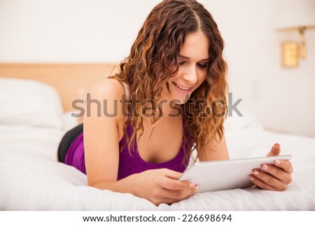 Cute young brunette using a tablet computer to read while relaxing in a hotel room
