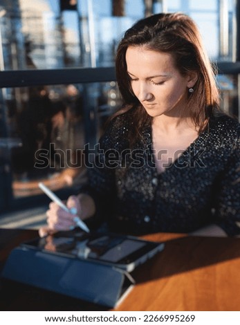 Female young digital artist illustrator drawing digital picture on a graphics tablet with pen stylus in cafe in a sunny day, freelance graphic designer working remotely and sketching with a pencil