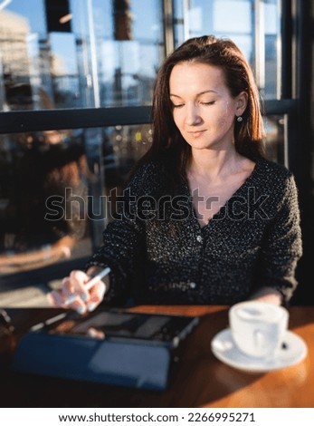 Female young digital artist illustrator drawing digital picture on a graphics tablet with pen stylus in cafe in a sunny day, freelance graphic designer working remotely and sketching with a pencil