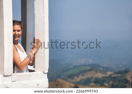 Pretty young woman smiling on balcony in Ambuluwawa tower of Sri Lankan mountains at nature background. Cute lady traveler enjoying at tropical journey, Gampola, Sri Lanka. Copy advertising text space