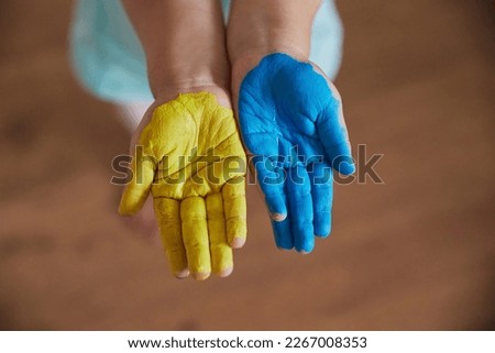 A cute child painted his hands in the colors of the Ukrainian flag